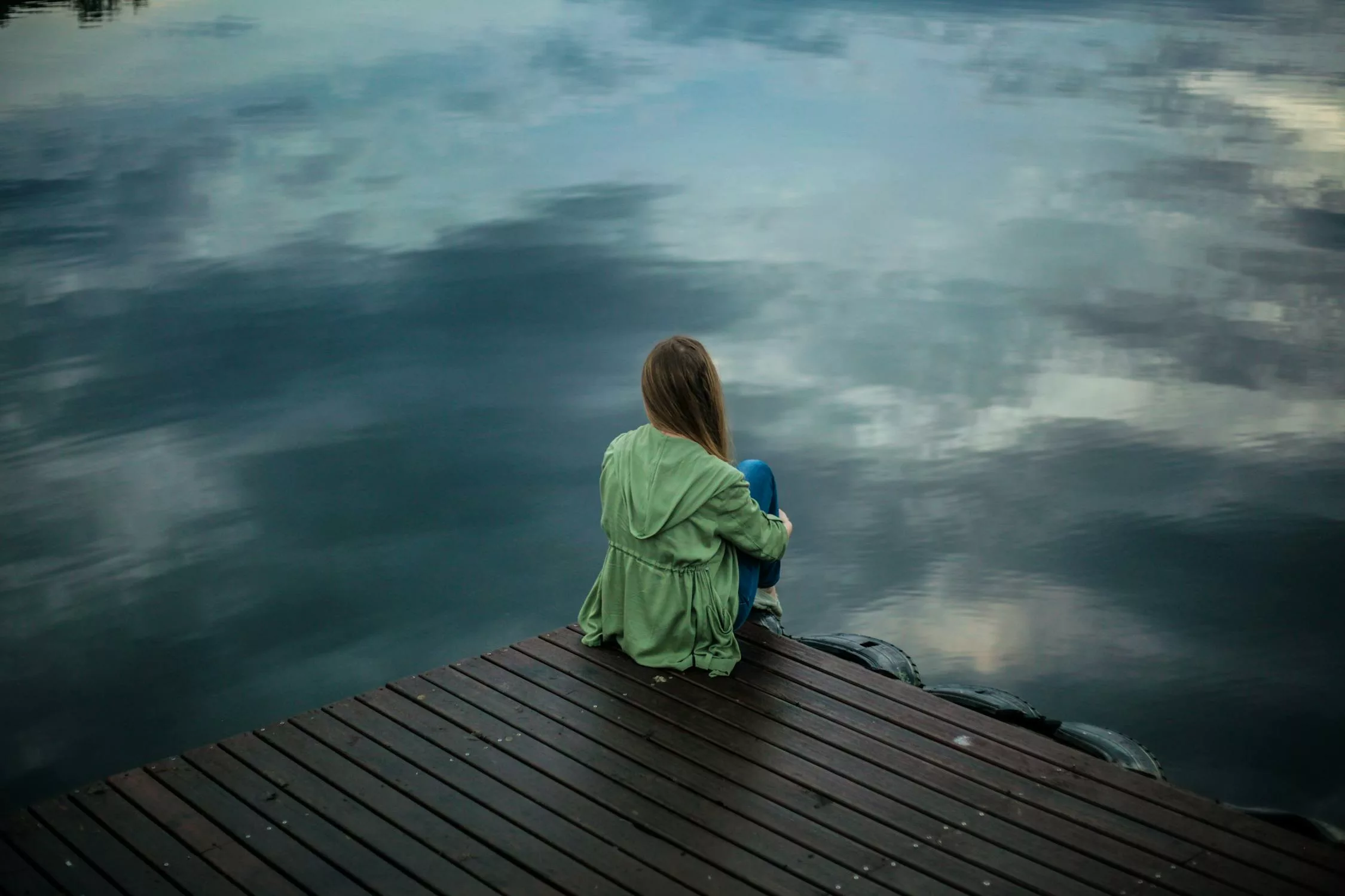 Woman sitting peacefully by a calm lake, reflecting on her emotions after an EFT tapping session